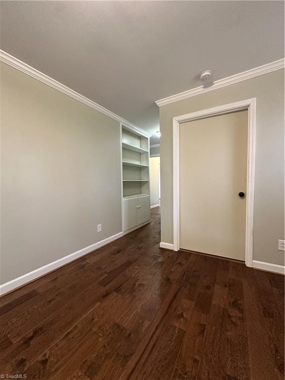 empty room featuring ornamental molding, dark wood-type flooring, and baseboards