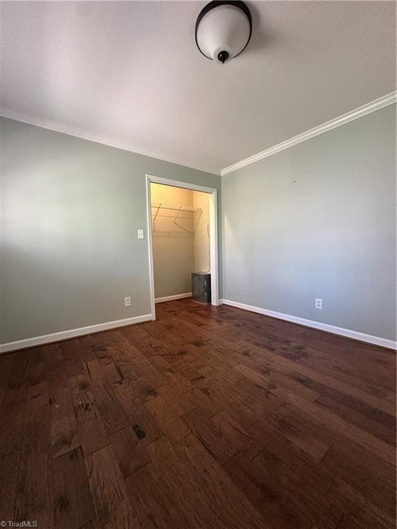 spare room featuring dark wood-style floors, ornamental molding, and baseboards