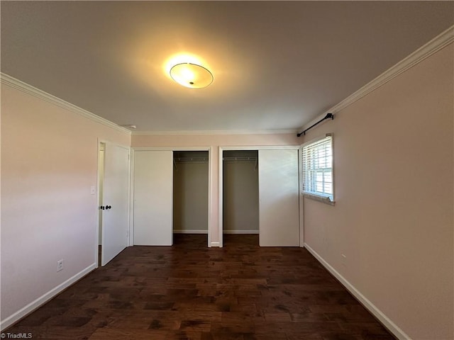 unfurnished bedroom with baseboards, ornamental molding, dark wood finished floors, and multiple closets