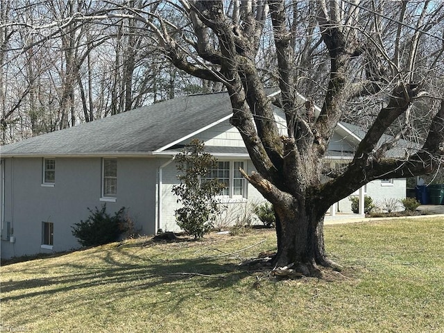 view of side of property featuring roof with shingles, a lawn, and stucco siding