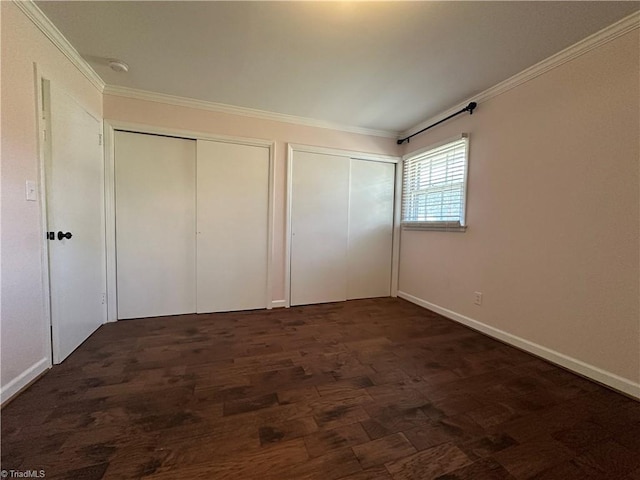 unfurnished bedroom with dark wood-style floors, baseboards, ornamental molding, and two closets