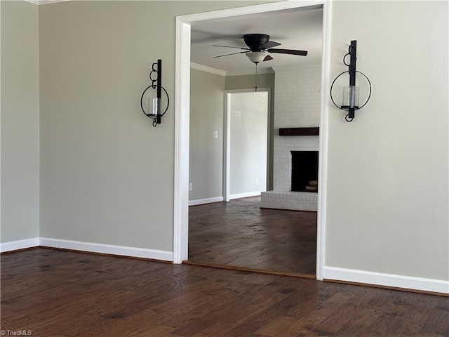 unfurnished room featuring baseboards, dark wood finished floors, ceiling fan, ornamental molding, and a brick fireplace