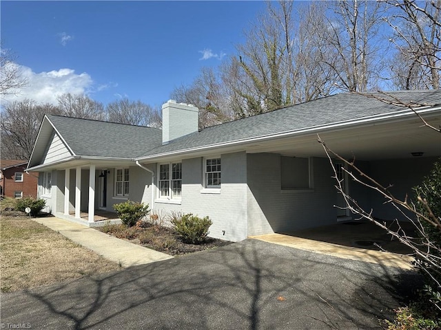 exterior space with driveway, a chimney, an attached carport, roof with shingles, and brick siding