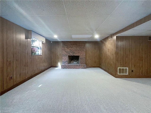 basement featuring wooden walls, a fireplace, a paneled ceiling, and light colored carpet