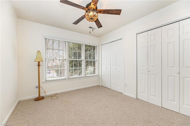 unfurnished bedroom with two closets, light carpet, and ceiling fan