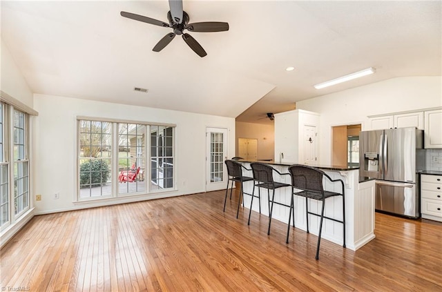 kitchen featuring light hardwood / wood-style flooring, stainless steel fridge, a kitchen breakfast bar, white cabinets, and vaulted ceiling