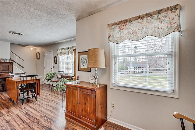 interior space featuring baseboards, a textured ceiling, visible vents, and wood finished floors