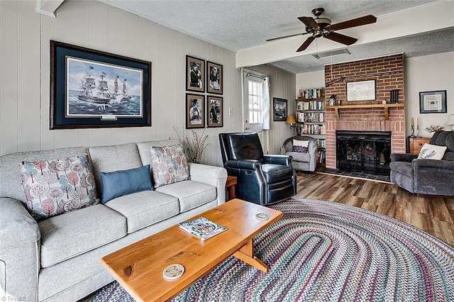 living area featuring visible vents, a brick fireplace, ceiling fan, a textured ceiling, and wood finished floors