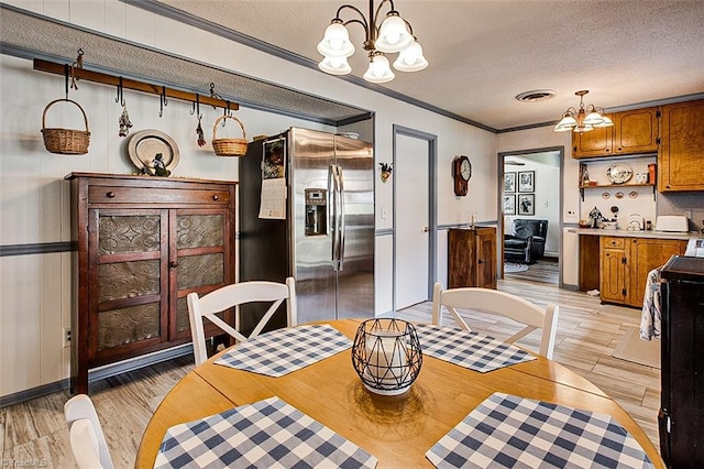 dining area with a textured ceiling, ornamental molding, light wood-style flooring, and a notable chandelier