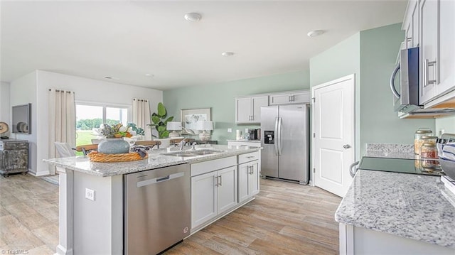 kitchen with light hardwood / wood-style flooring, appliances with stainless steel finishes, a kitchen island with sink, light stone countertops, and white cabinets