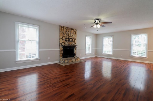 unfurnished living room with a stone fireplace, dark hardwood / wood-style flooring, and ceiling fan