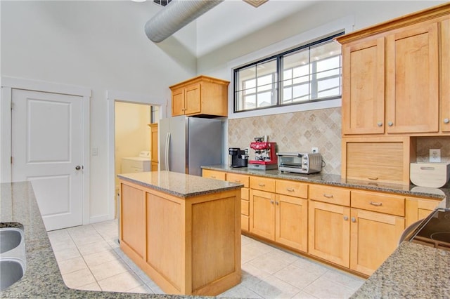 kitchen featuring stainless steel refrigerator, light stone countertops, decorative backsplash, and a center island