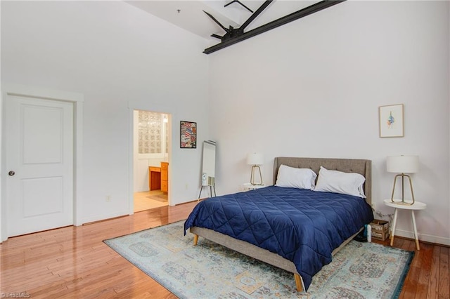 bedroom featuring ceiling fan, hardwood / wood-style flooring, ensuite bath, and a towering ceiling