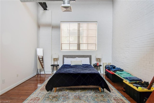 bedroom featuring brick wall and hardwood / wood-style flooring