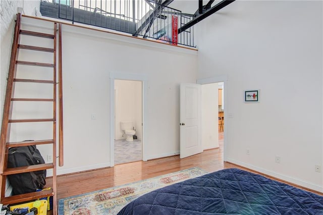 bedroom featuring a high ceiling, connected bathroom, and hardwood / wood-style flooring