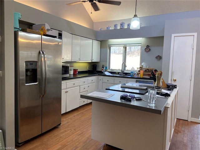 kitchen featuring dark countertops, vaulted ceiling, stainless steel appliances, white cabinetry, and a sink