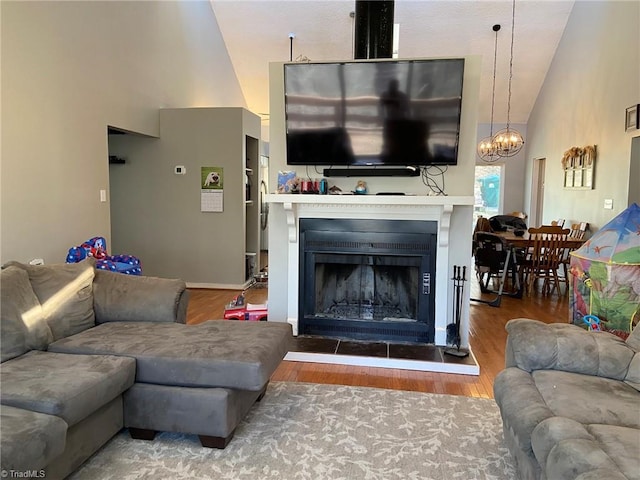 living room with a fireplace with raised hearth, wood finished floors, and high vaulted ceiling