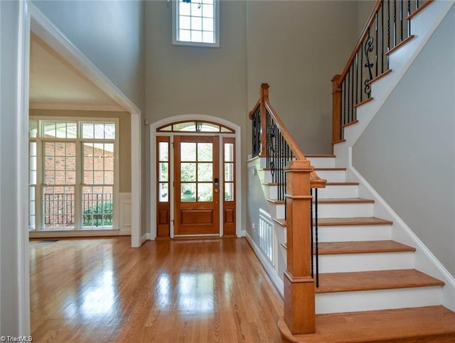 foyer entrance with wood finished floors, stairway, a towering ceiling, wainscoting, and a decorative wall