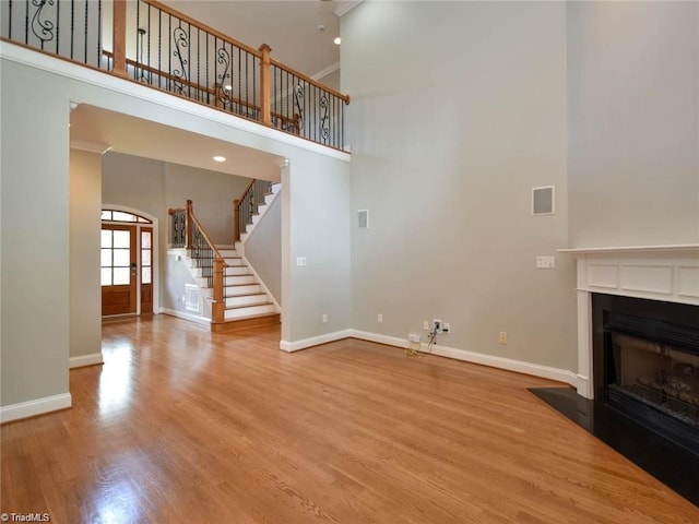 unfurnished living room featuring stairway, baseboards, a high ceiling, wood finished floors, and a fireplace with flush hearth