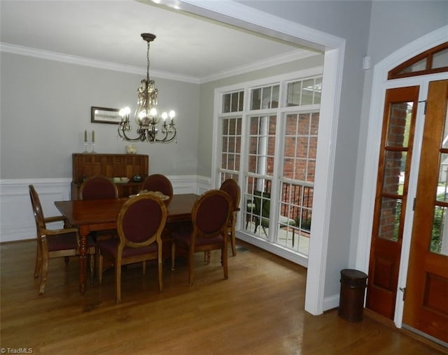 dining space featuring a chandelier, ornamental molding, wood finished floors, and a wainscoted wall