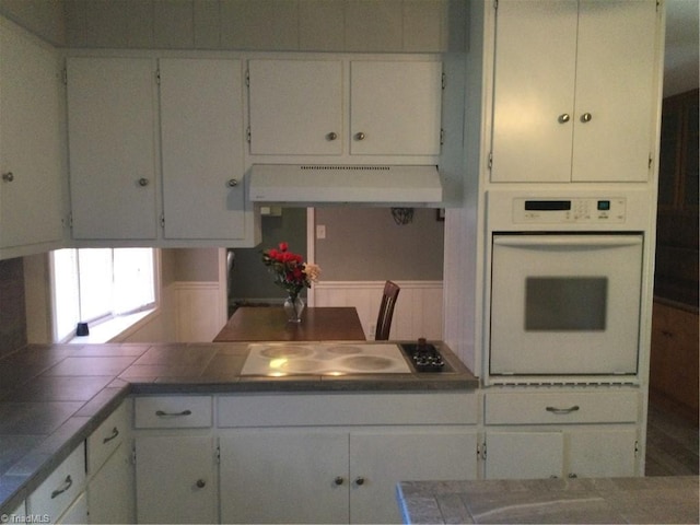 kitchen with tile countertops, electric cooktop, range hood, white cabinets, and white oven