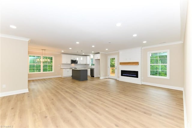 unfurnished living room featuring a large fireplace, ornamental molding, and light wood-type flooring