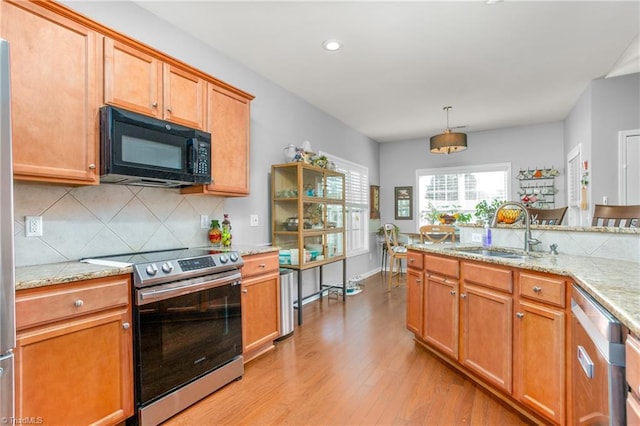 kitchen featuring decorative light fixtures, sink, light stone counters, light hardwood / wood-style floors, and stainless steel appliances