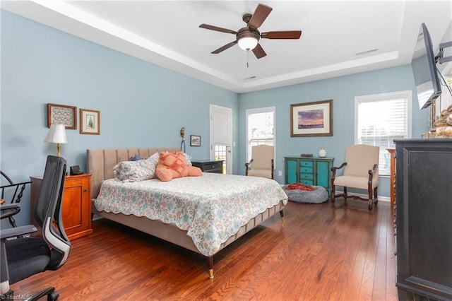 bedroom featuring dark wood-type flooring, ceiling fan, a raised ceiling, and multiple windows