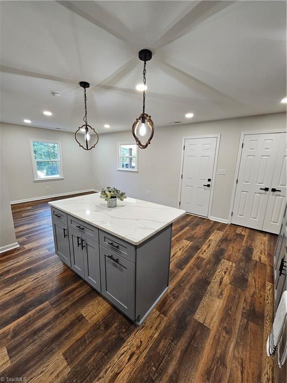 kitchen with hanging light fixtures, a kitchen island, gray cabinets, light stone countertops, and dark hardwood / wood-style flooring