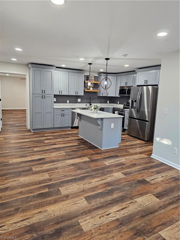 kitchen featuring dark hardwood / wood-style floors, hanging light fixtures, gray cabinetry, backsplash, and appliances with stainless steel finishes