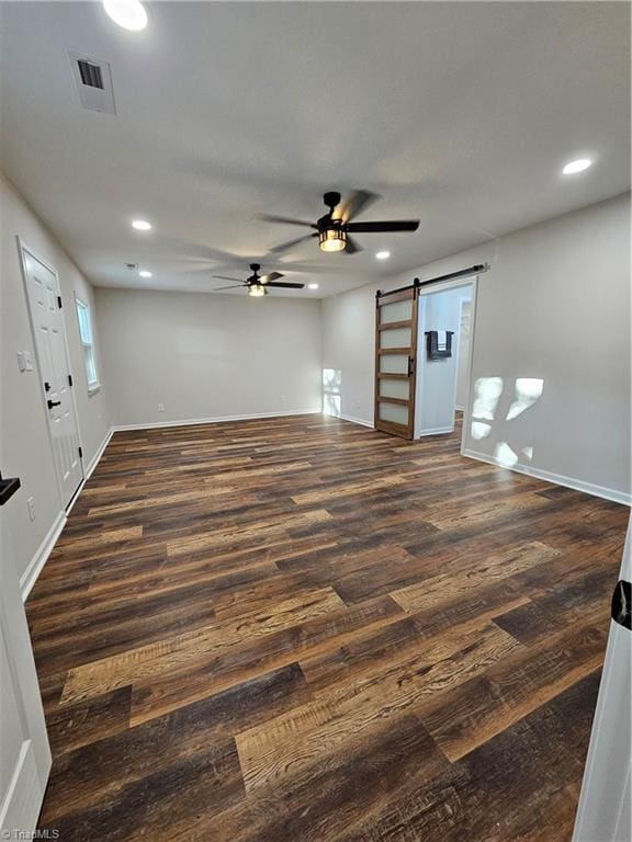 unfurnished living room with ceiling fan, dark hardwood / wood-style floors, and a barn door