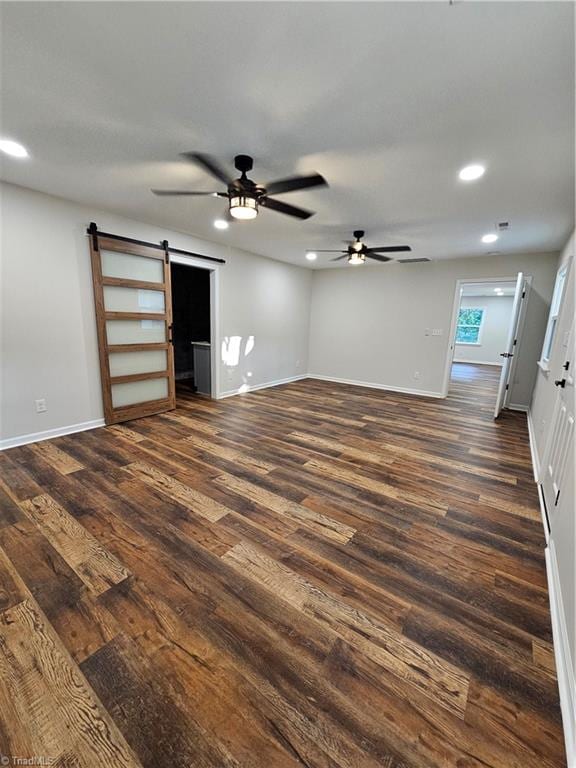 unfurnished living room featuring ceiling fan, dark hardwood / wood-style floors, and a barn door