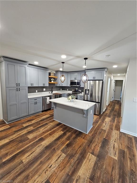 kitchen with appliances with stainless steel finishes, dark wood-type flooring, tasteful backsplash, gray cabinets, and decorative light fixtures