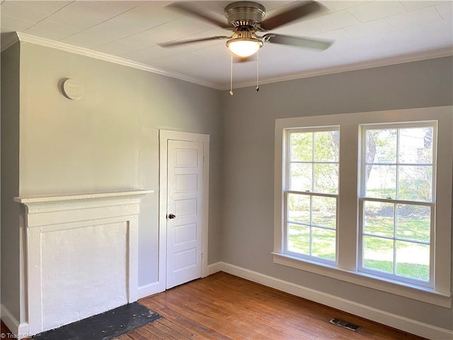 spare room with a wealth of natural light, wood-type flooring, crown molding, and baseboards