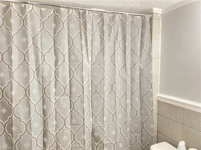 full bathroom with a textured ceiling, toilet, tile walls, wainscoting, and a shower with curtain