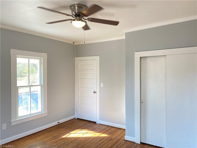 unfurnished bedroom featuring baseboards, a ceiling fan, wood finished floors, crown molding, and a closet