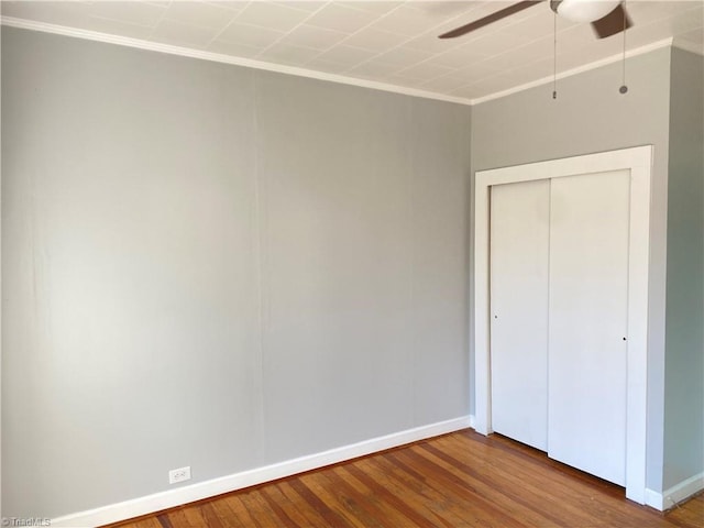 unfurnished bedroom featuring wood finished floors, a ceiling fan, baseboards, ornamental molding, and a closet