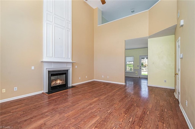 unfurnished living room featuring a towering ceiling, a fireplace, baseboards, and wood finished floors