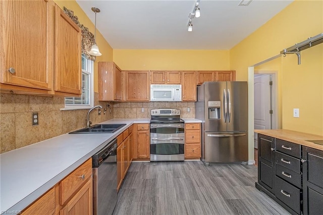 kitchen with a sink, backsplash, wood finished floors, stainless steel appliances, and light countertops