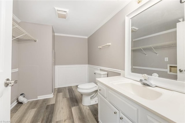 bathroom with a wainscoted wall, toilet, ornamental molding, vanity, and wood finished floors