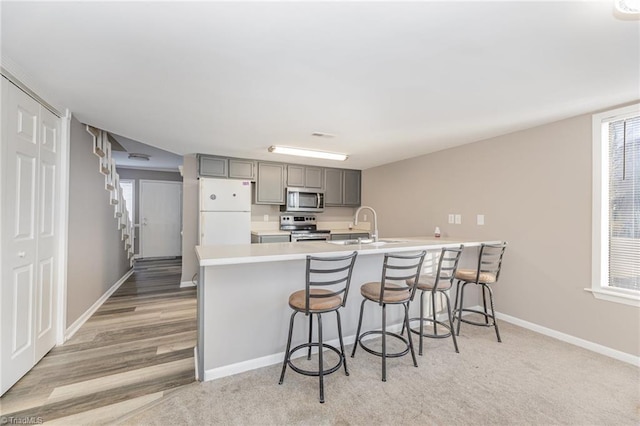 kitchen featuring stainless steel appliances, a sink, light countertops, gray cabinets, and a kitchen bar