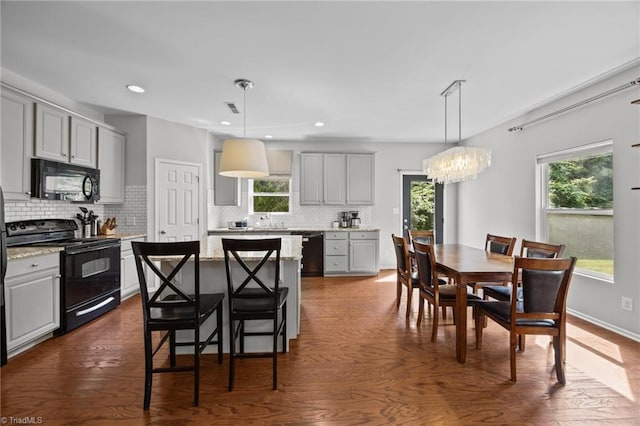 kitchen with black appliances, gray cabinetry, a chandelier, decorative backsplash, and a kitchen island