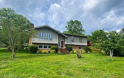 split foyer home featuring brick siding, a front lawn, and a chimney