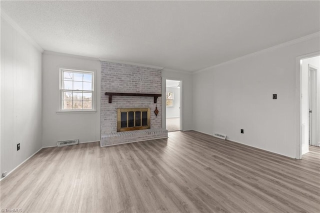 unfurnished living room with light hardwood / wood-style floors, a textured ceiling, ornamental molding, and a fireplace