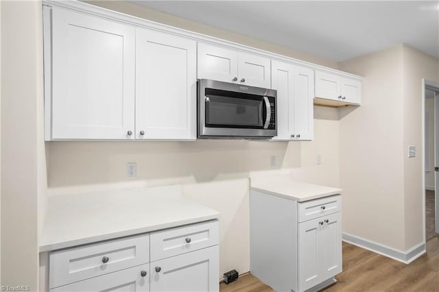 kitchen featuring stainless steel microwave, white cabinets, light countertops, and light wood-type flooring