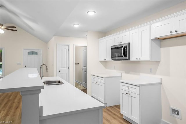 kitchen with a kitchen island with sink, a sink, stainless steel microwave, light wood finished floors, and ceiling fan