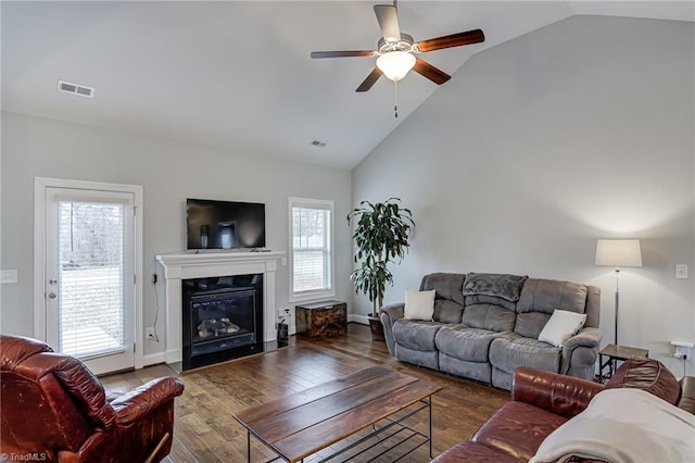 living area with high vaulted ceiling, wood finished floors, visible vents, a ceiling fan, and a glass covered fireplace