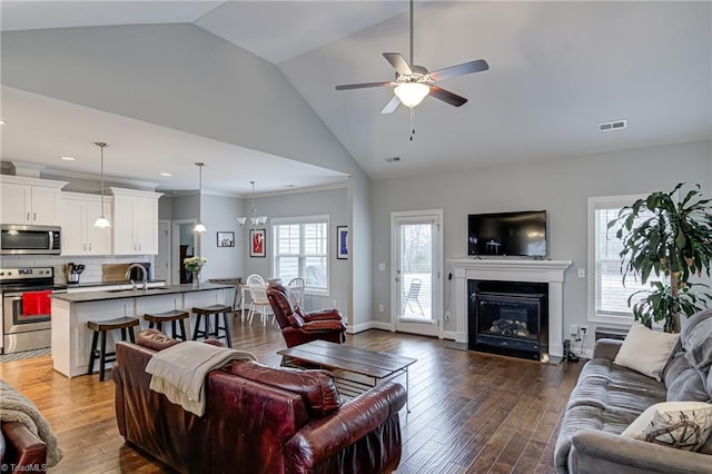 living area with visible vents, a ceiling fan, a glass covered fireplace, wood finished floors, and baseboards