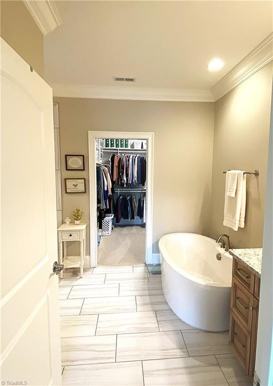 full bath featuring vanity, visible vents, a soaking tub, ornamental molding, and a walk in closet