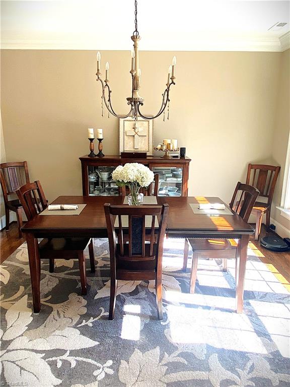 dining area with crown molding, wood finished floors, visible vents, and baseboards